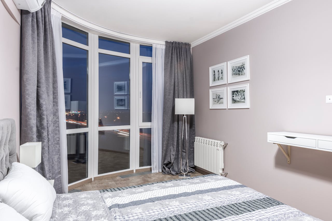 Elegant bedroom with large windows overlooking city lights, featuring a stylish decor and a cozy ambiance.