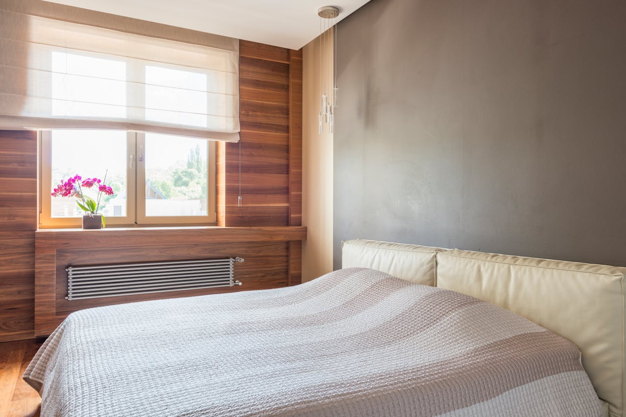 A cozy modern bedroom featuring natural light, wooden accents, and a vibrant orchid plant.